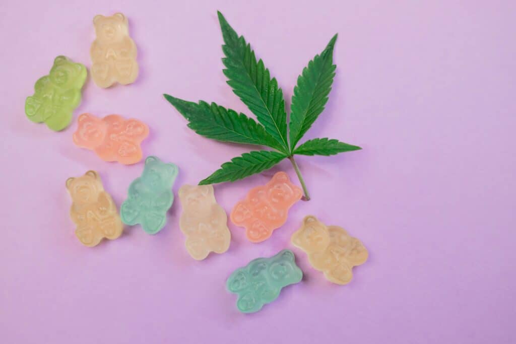 Vibrant gummy bears and a cannabis leaf on a pastel background, symbolizing cannabis edibles.